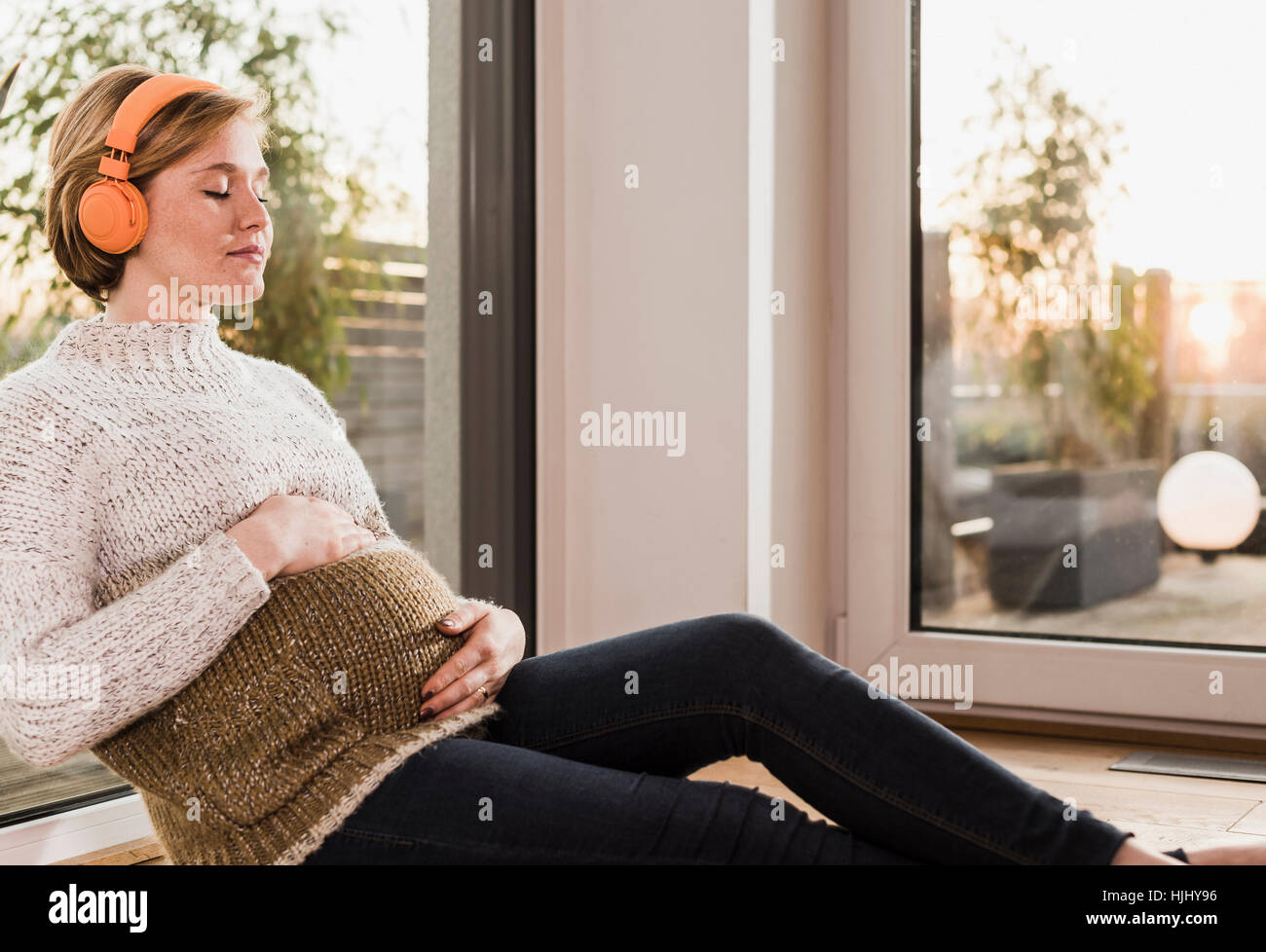 Pregnant woman sitting on floor listening to music Stock Photo - Alamy