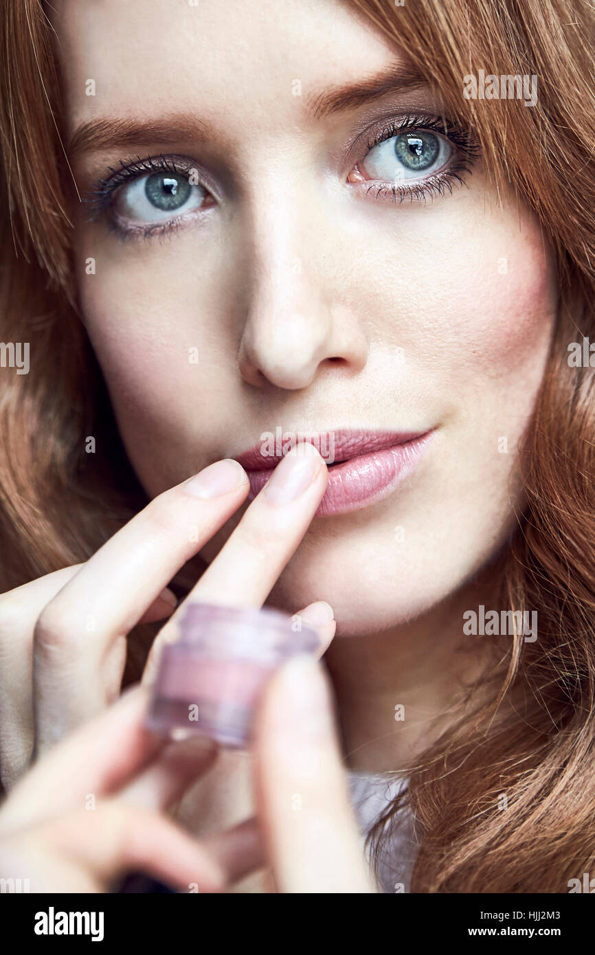 Portrait of redheaded woman applying cream on her lips Stock Photo