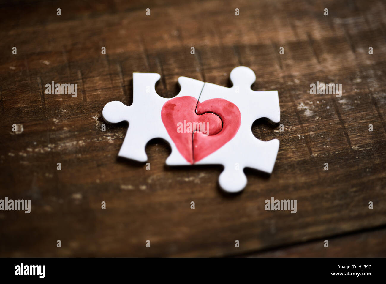 closeup of two pieces of a puzzle forming a heart on a rustic wooden surface, depicting the idea of that love is a thing of two Stock Photo