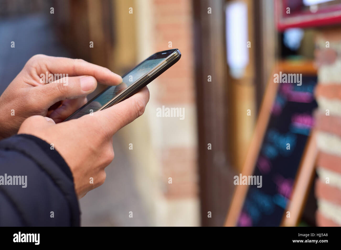 closeup of a young caucasian man using a smartphone in the street, in front of a restaurant Stock Photo