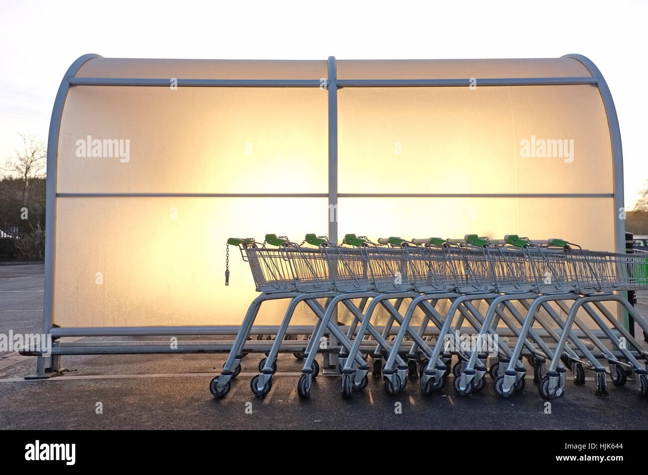 The sun rises behind a trolley bay in an Asda carpark. Stock Photo