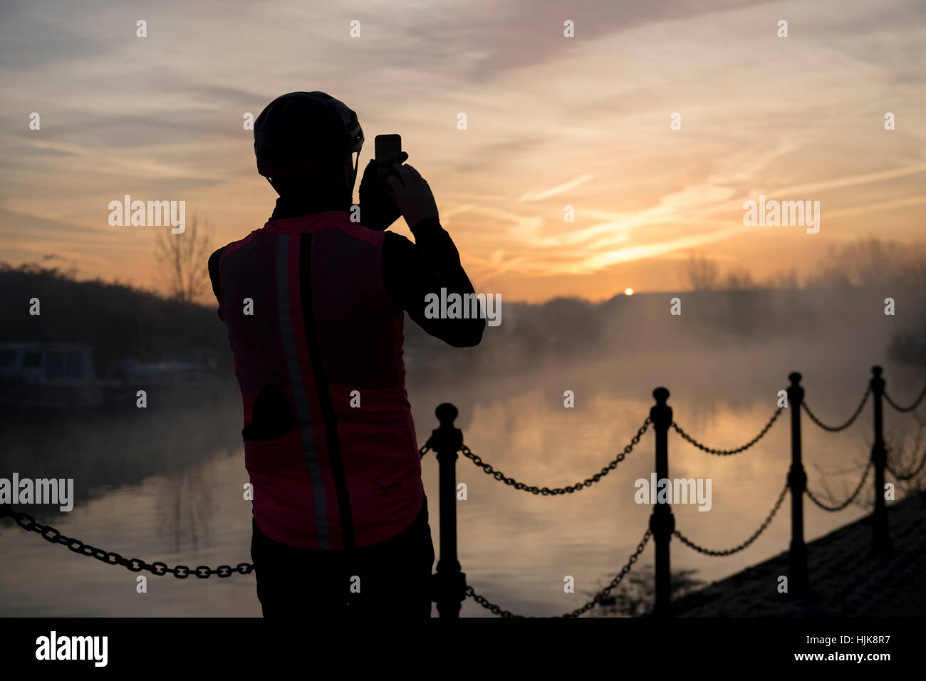 A cyclist takes a photograph of the sunrise over the River Lea, in Hackney north London Stock Photo