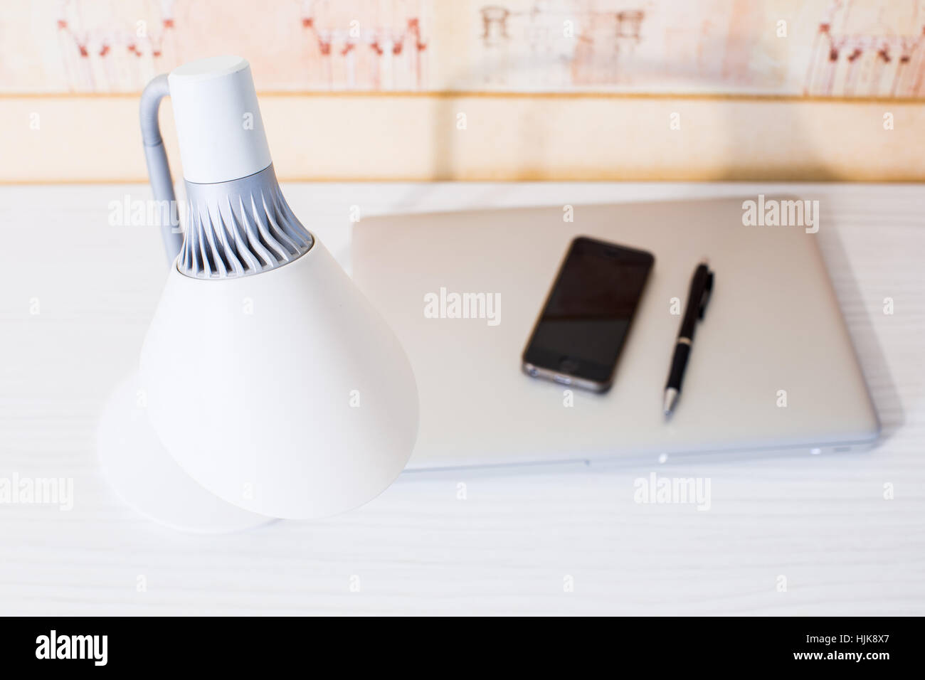 Home workspace with table lamp, macbook, phone and pen. White table. Stock Photo