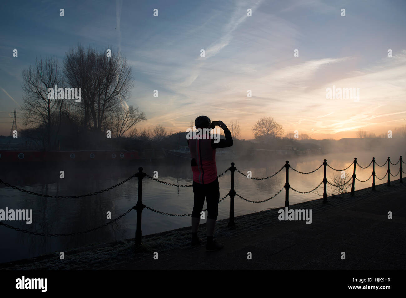 A cyclist takes a photograph of the sunrise over the River Lea, in Hackney north London Stock Photo