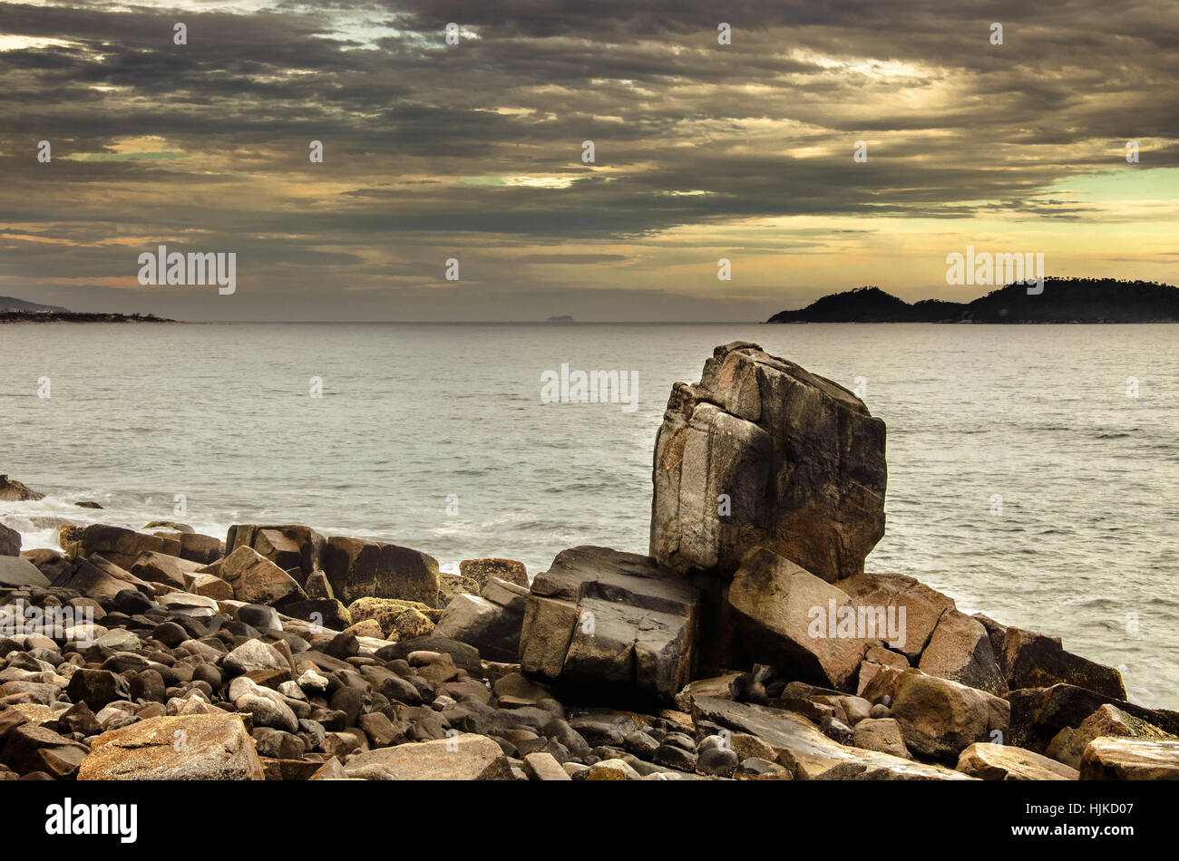 Large pointed stone among the rocky formations by the sea. Golden hour sunset with some islands on the background. Morro das Pedras, Florianopolis, Br Stock Photo