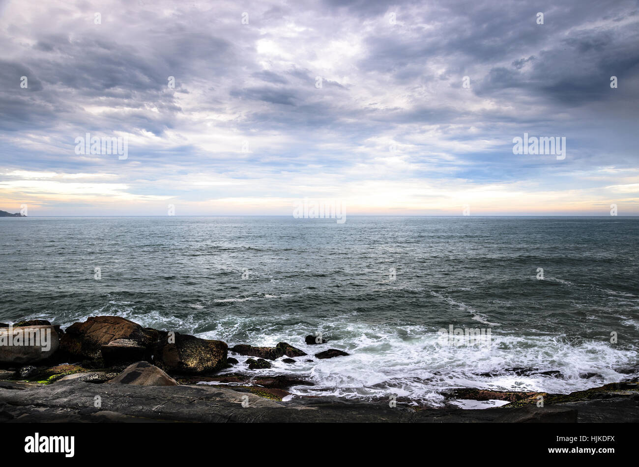 Sea water running over the rocks on sea shore. Large rocks, many clouds, and the horizon on a beautiful seascape, wonderful scene at Morro das Pedras, Stock Photo