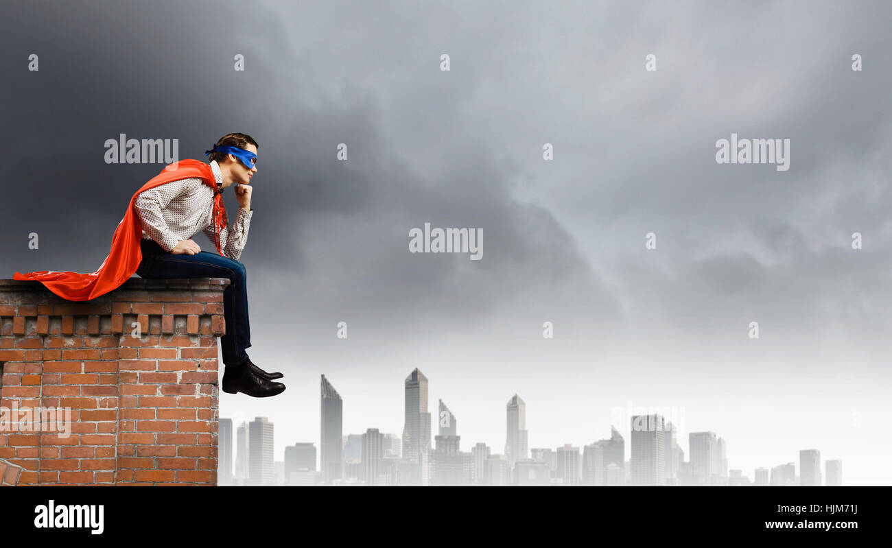 Young man in superhero costume sitting on top of building hi-res stock ...