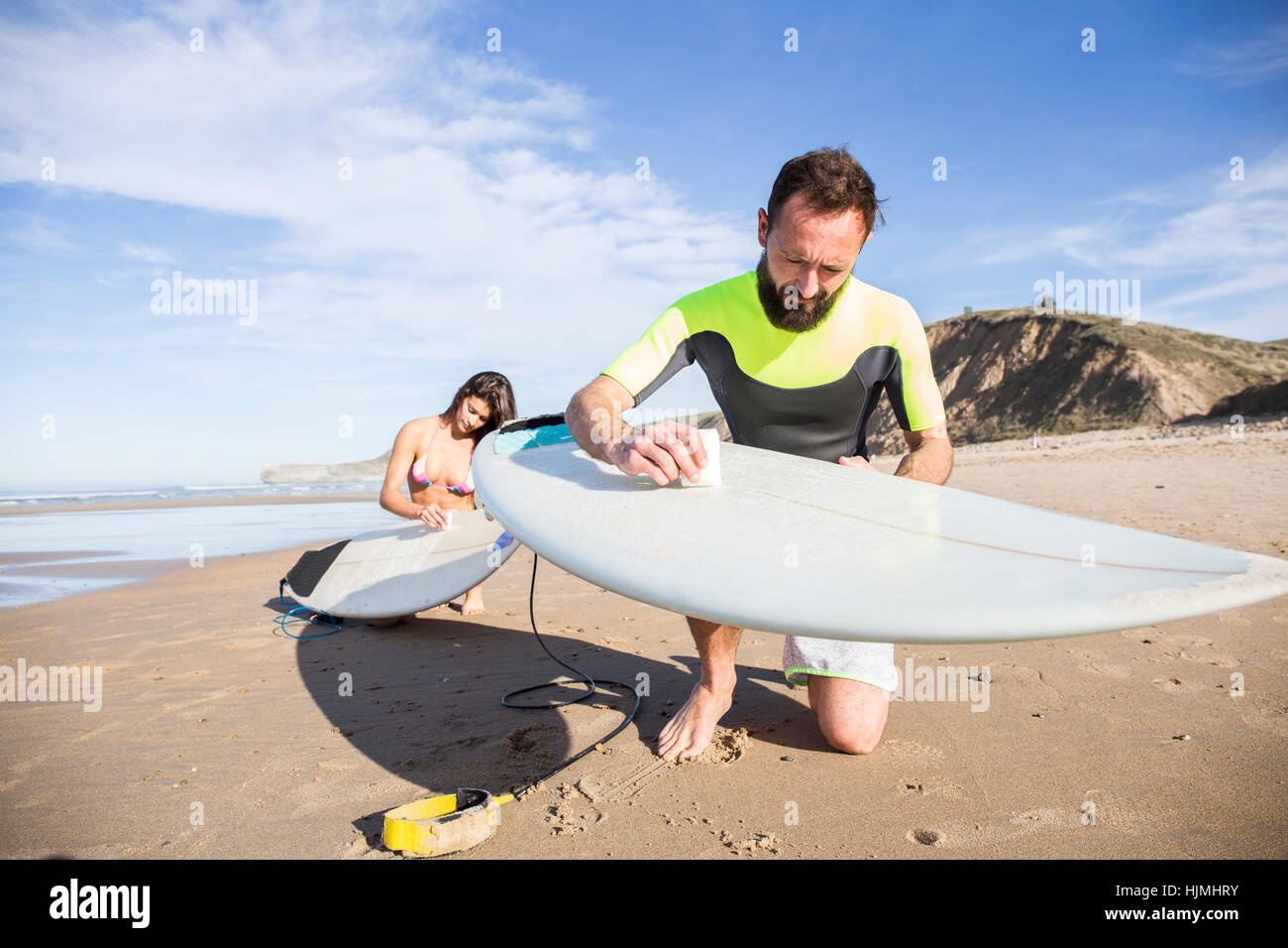 Couple putting paraffin on their surfboards on the beach Stock Photo