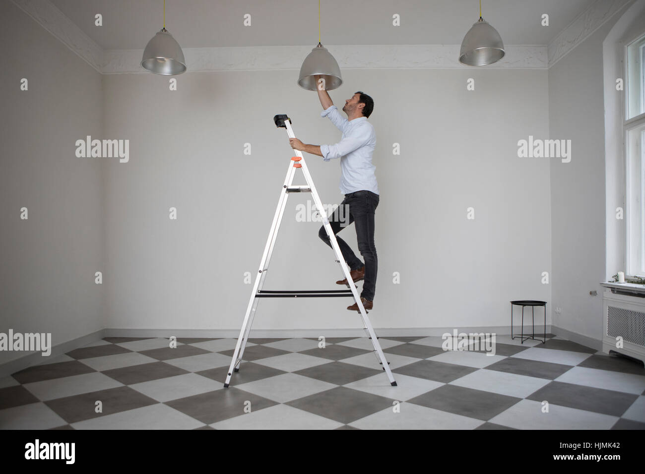 Man Standing On Ladder In An Empty Room Changing Bulb Of