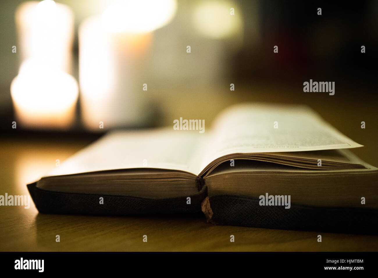 Bible laid on wooden floor, burning candles in the background Stock Photo