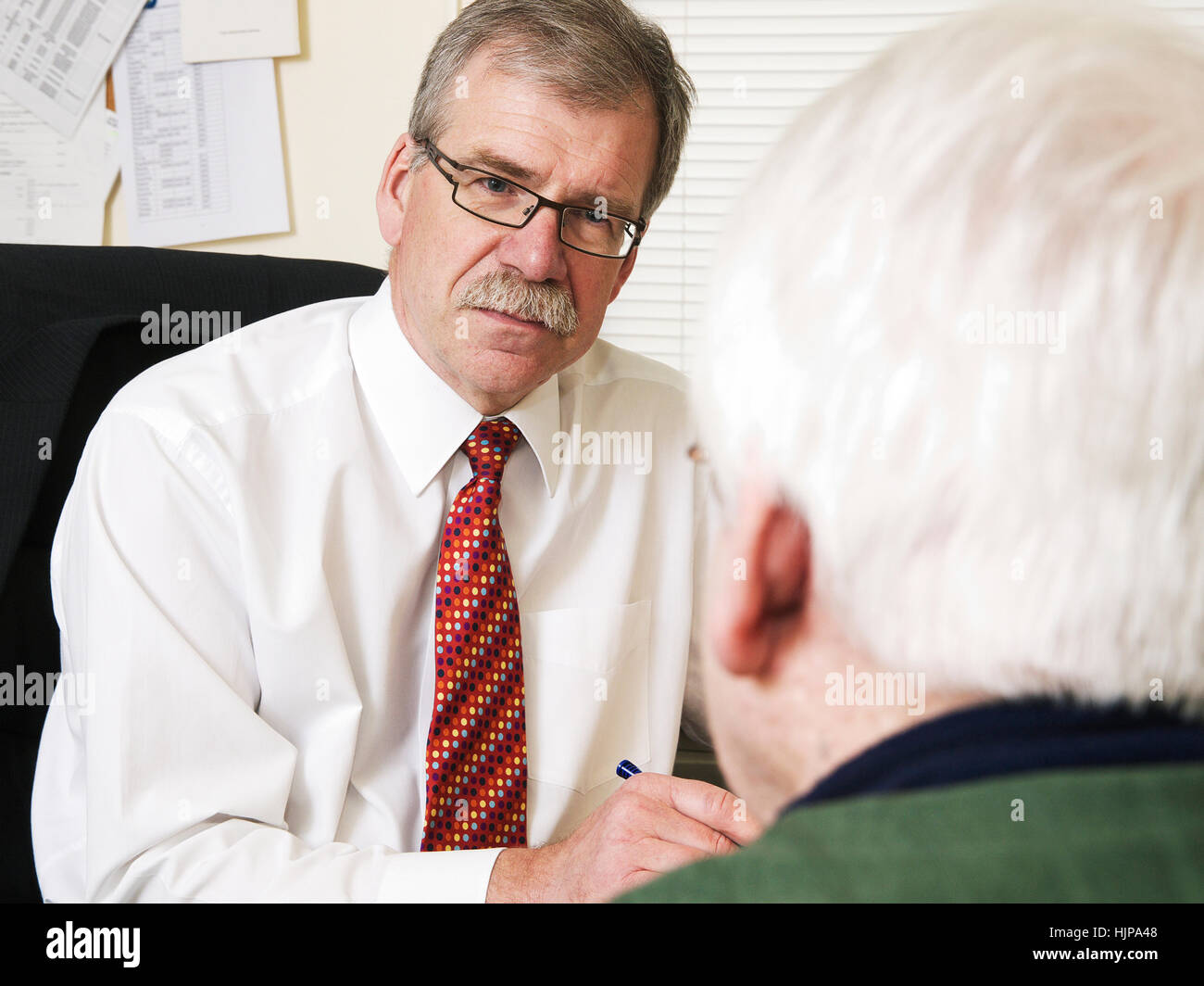 Male GP talking to patient regarding blood test results at appointment at local GP health clinic Stock Photo