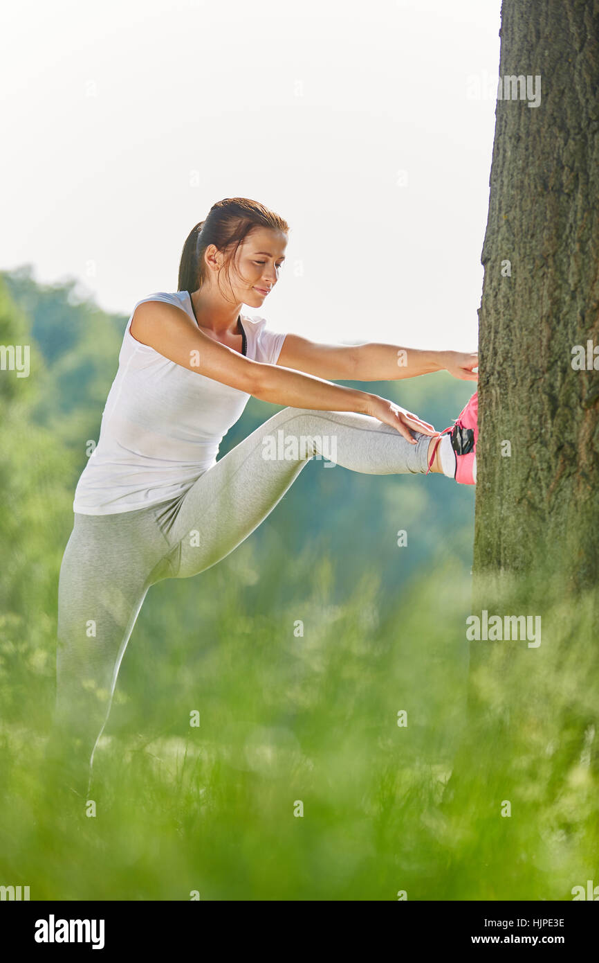 Young woman stretching on tree before running in the park Stock Photo