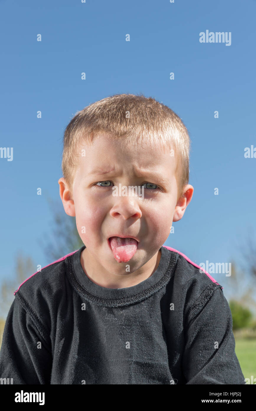 Naughty boy sticks out tongue outdoors. The park is green and the sky is Blue Stock Photo Alamy