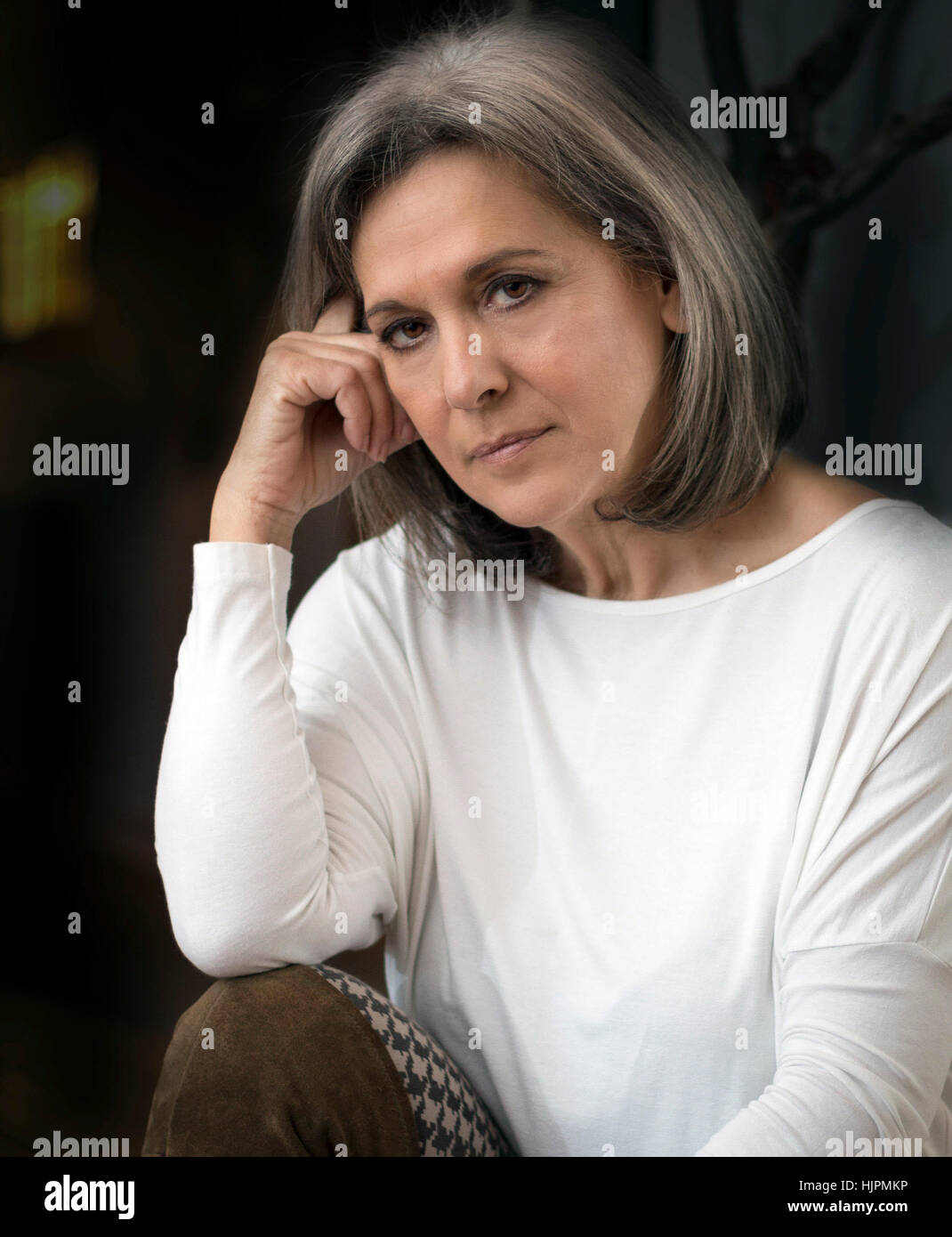 Mature Woman looking serious, thinking, arm on knee, hand on cheek. Stock Photo