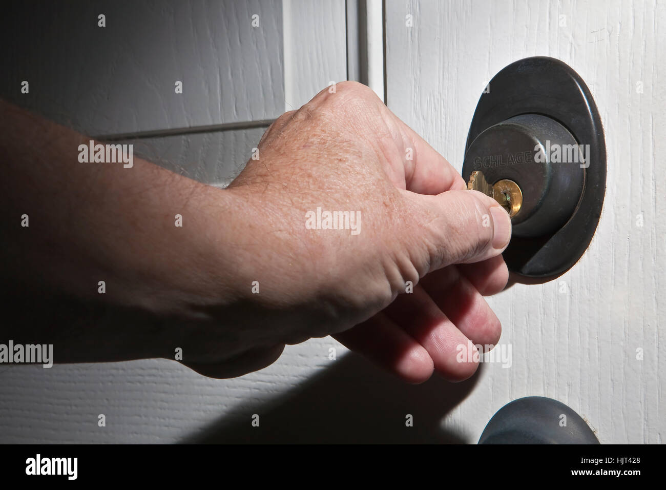 Older man's hand turning house key in lock of white door Stock Photo