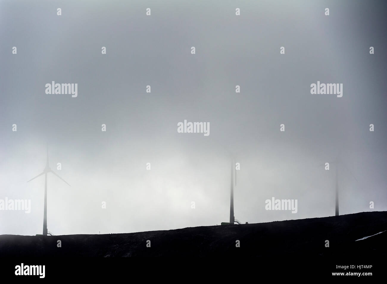 Wind turbines on a barren volcanic hill shrouded in cloud in Antarctica. Stock Photo