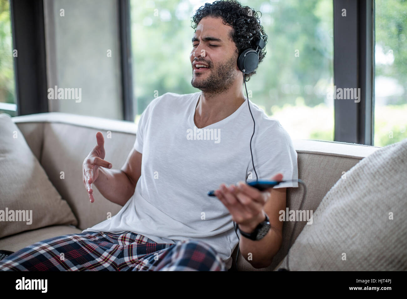 Young man sitting on couch listening to music Stock Photo - Alamy