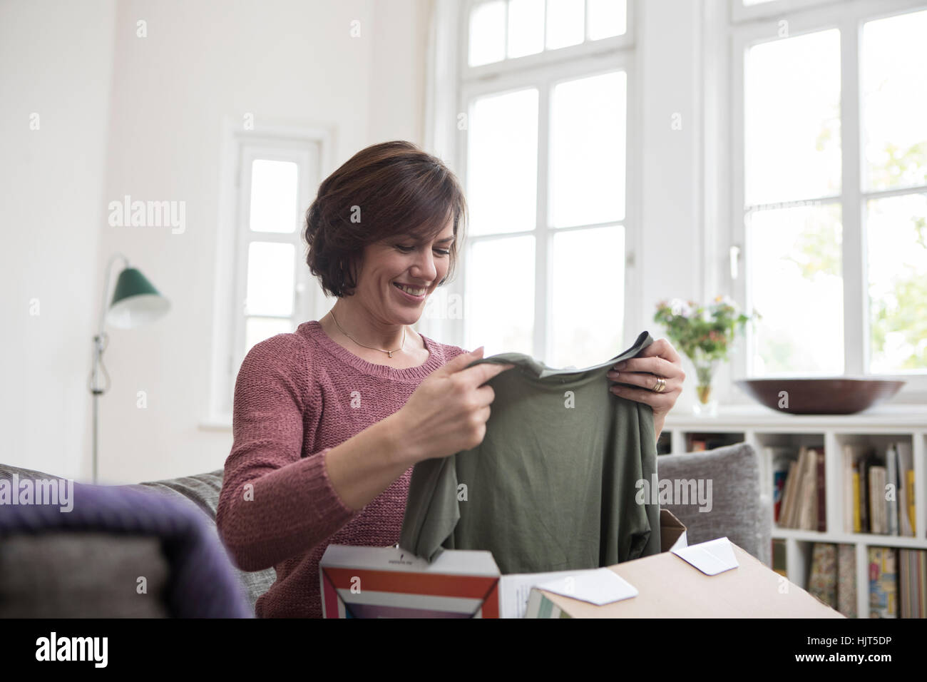 Smiling woman at home sitting on the sofa looking at garment Stock Photo