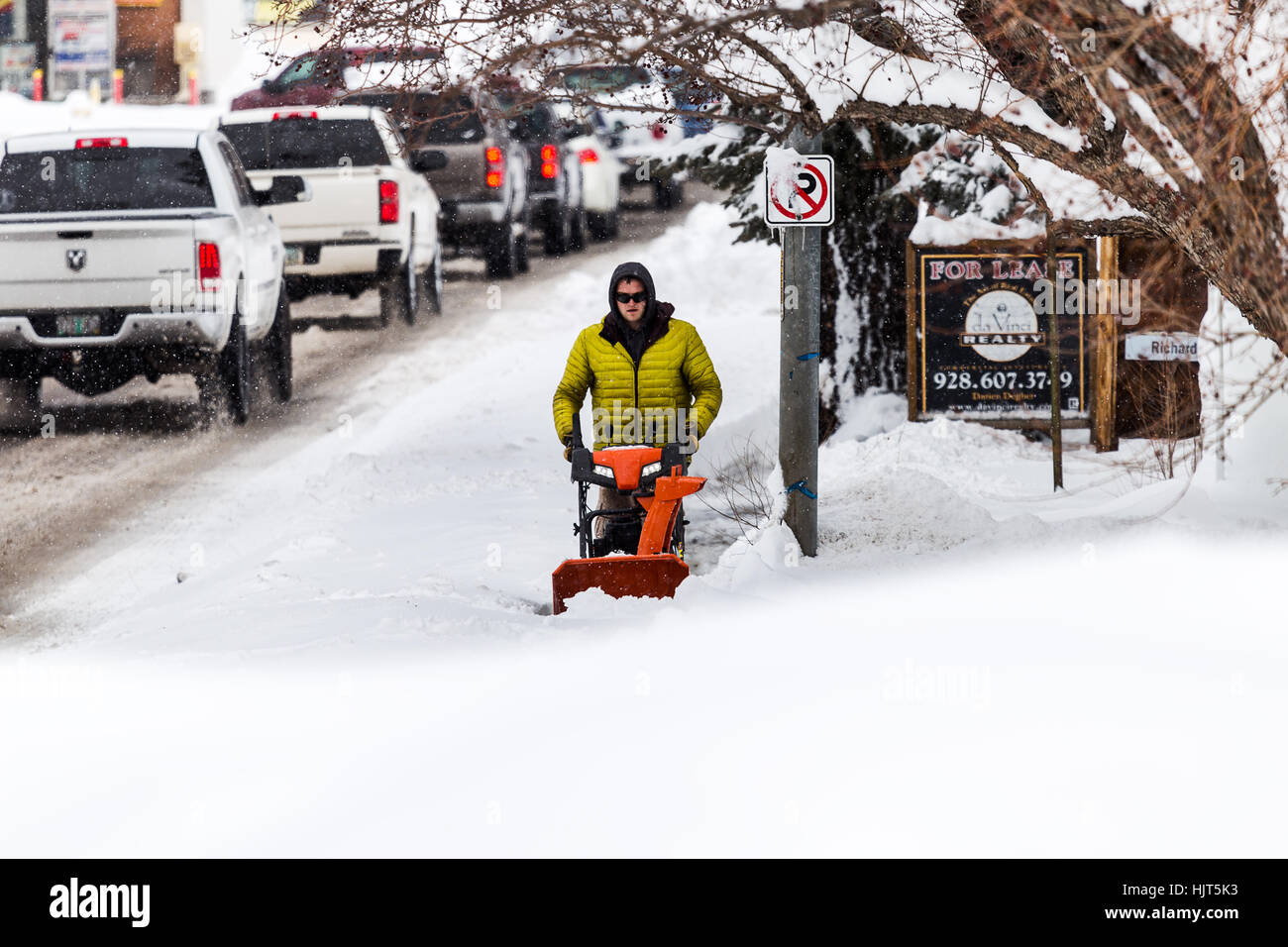 A man uses a snow blower to clear the sidewalk after a powerful winter snowstorm Stock Photo