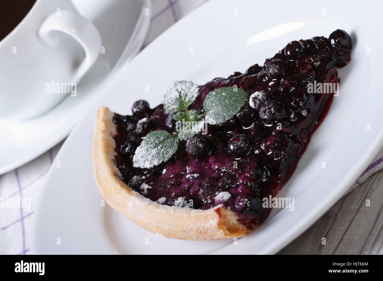 a piece of blueberry pie with mint and powdered sugar on a plate and coffee on the table horizontal closeup Stock Photo
