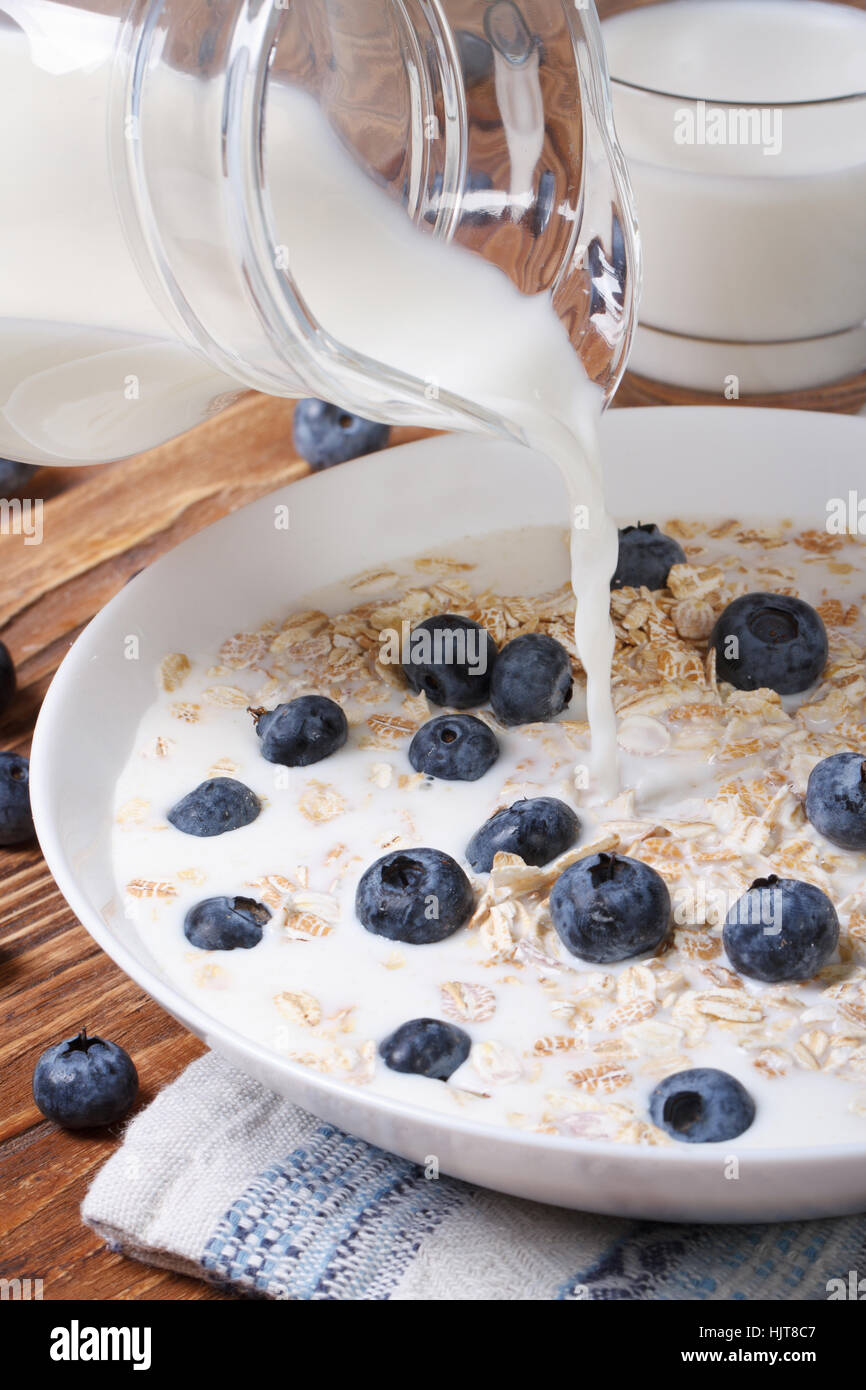 oatmeal with blueberries and milk is poured from a jug on the table closeup. vertical Stock Photo