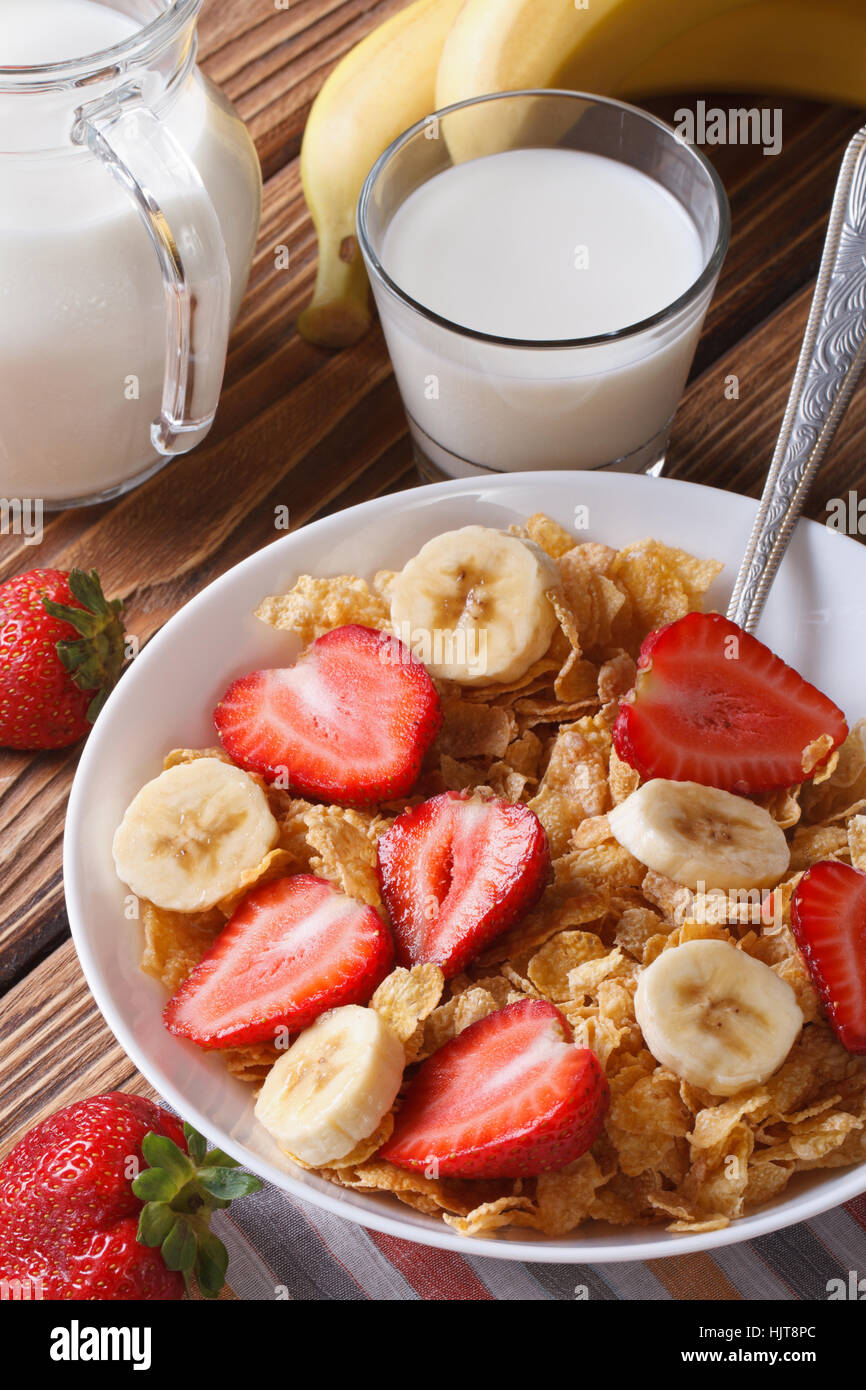 Cornflakes with fresh strawberries and a banana on the table and milk in a glass closeup. vertical Stock Photo