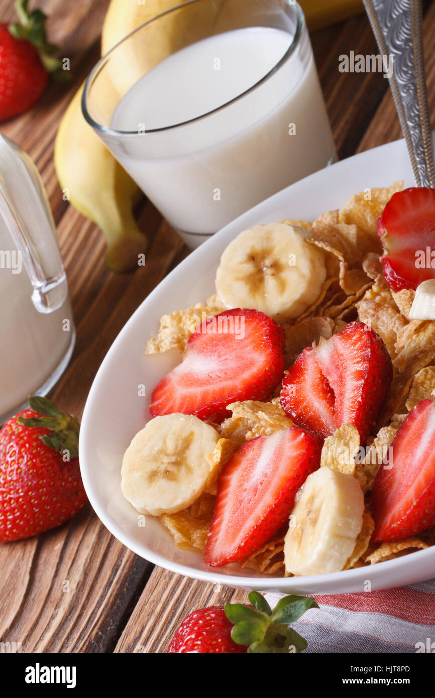 Cornflakes with fresh strawberries and banana close up on the table and milk. vertical Stock Photo