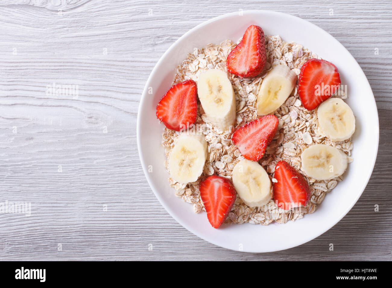 muesli with fresh strawberries and banana closeup on wooden background. horizontal top view Stock Photo