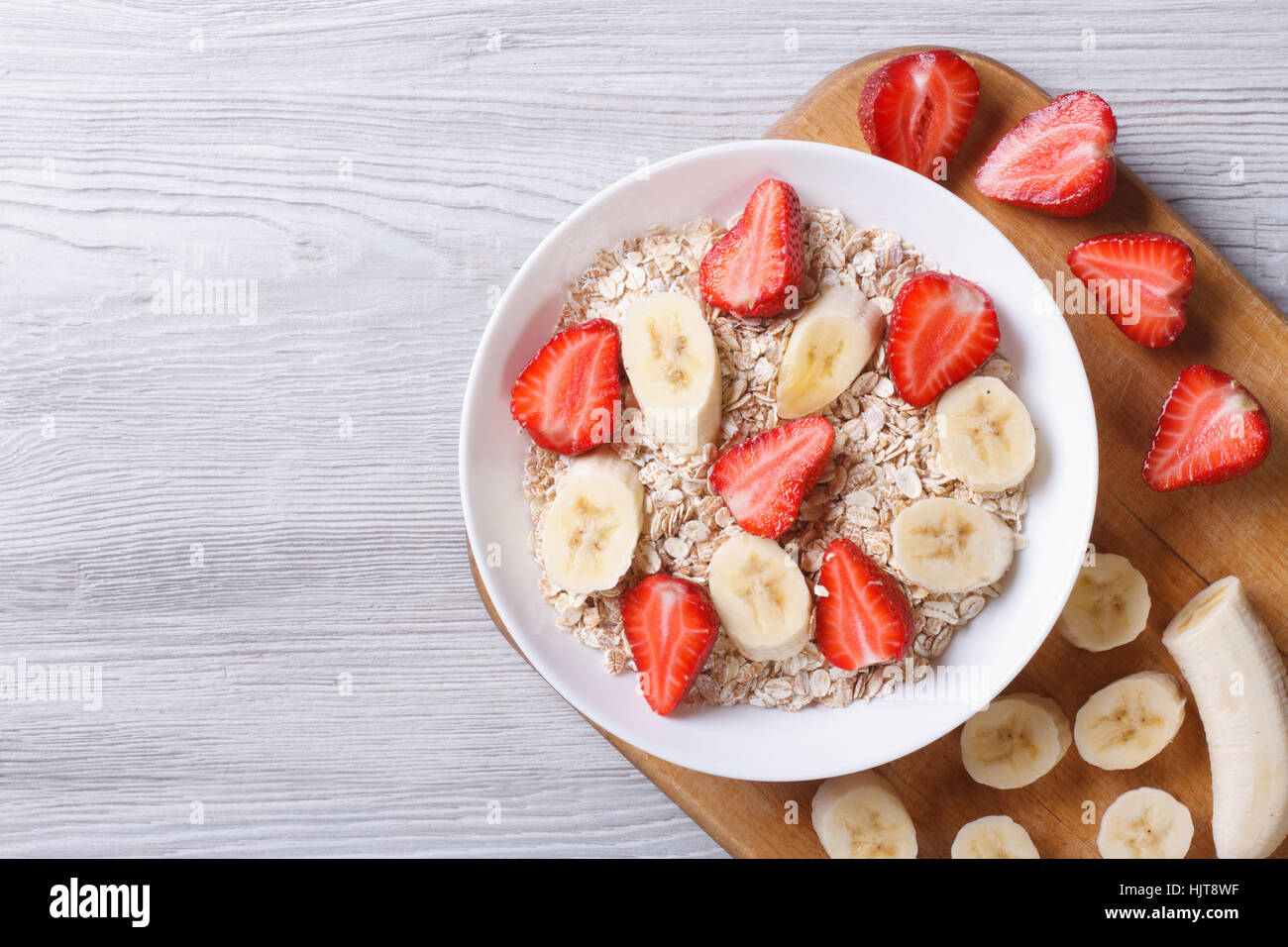 muesli with fresh strawberries and banana with chopped ingredients closeup on wooden background. horizontal top view Stock Photo