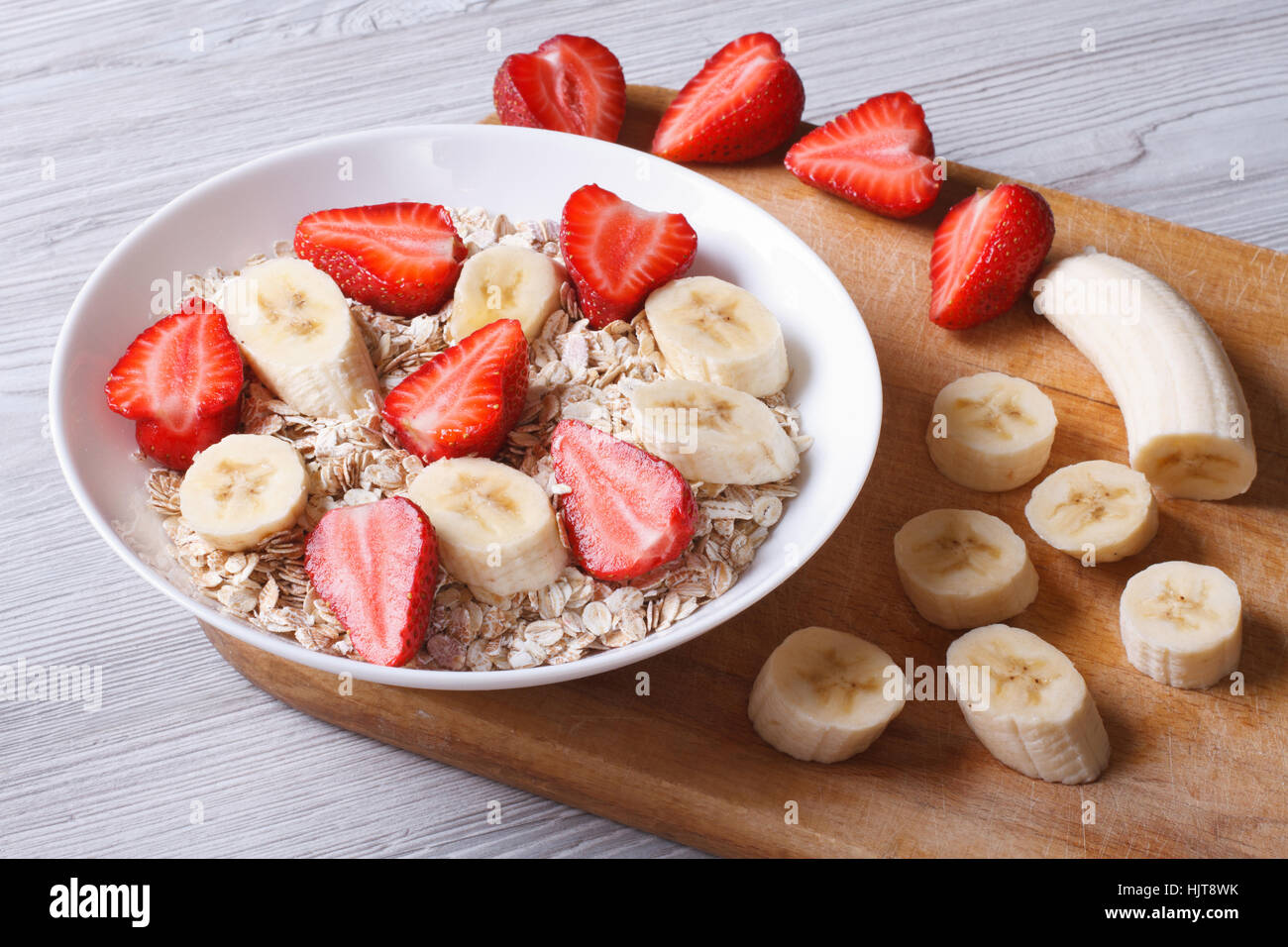 muesli with fresh strawberries and banana with chopped ingredients closeup on a wooden table. horizontal Stock Photo
