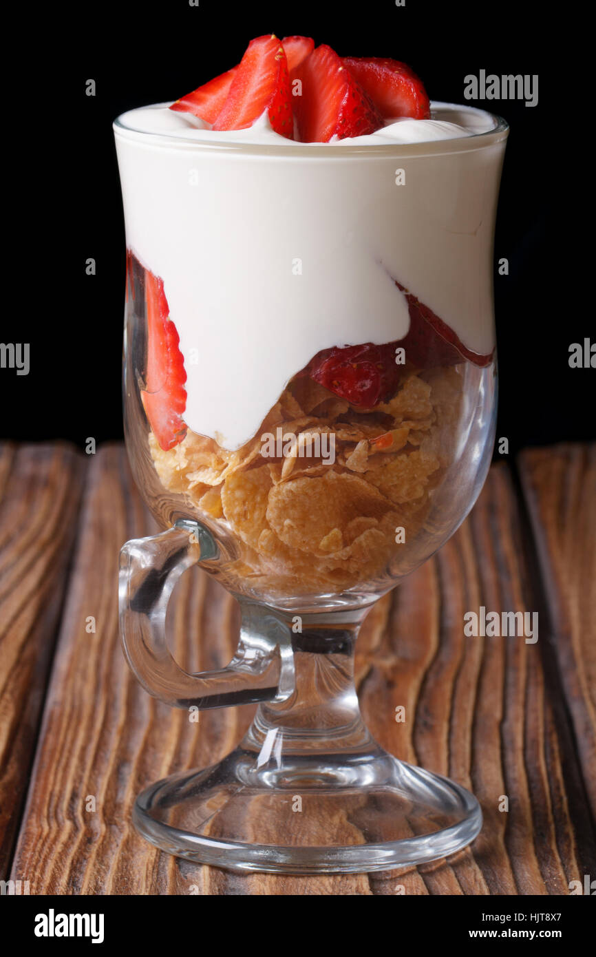 muesli with fresh strawberries and yogurt in a glass closeup on a wooden table. vertical. low key Stock Photo