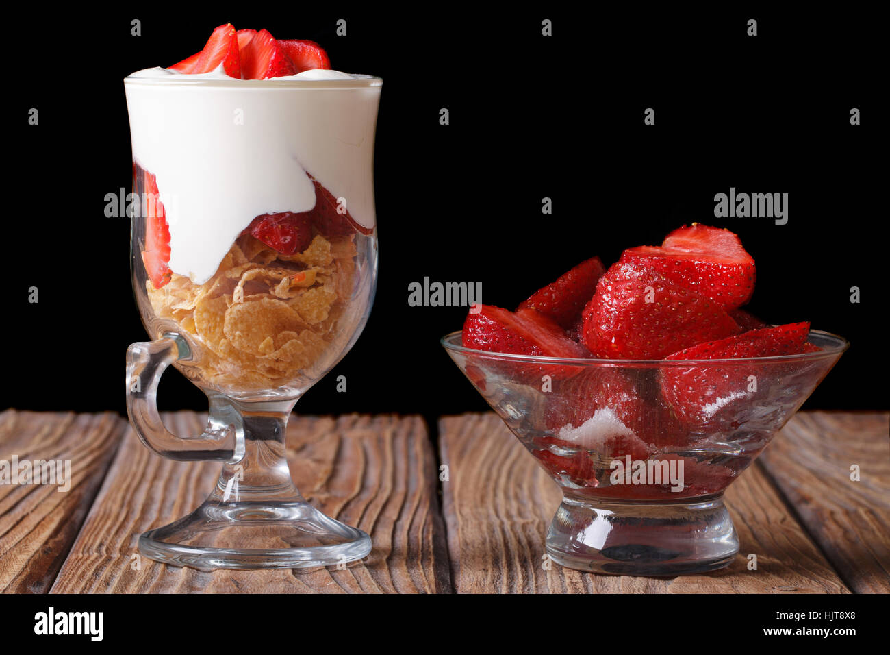 yogurt with strawberries and cornflakes in a glass closeup on a wooden table. horizontal. low key Stock Photo