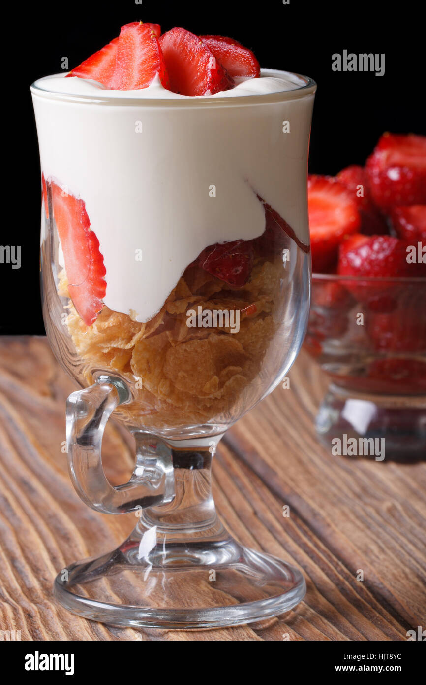 yogurt with strawberries and cornflakes in a glass closeup on a wooden table. vertical. low key Stock Photo