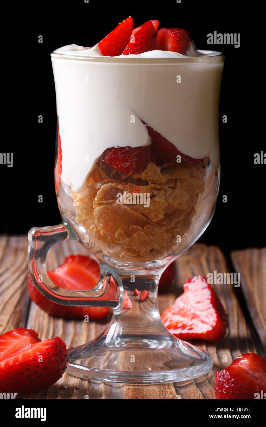 yogurt with fresh strawberries and cornflakes in a glass closeup on a dark background. vertical Stock Photo