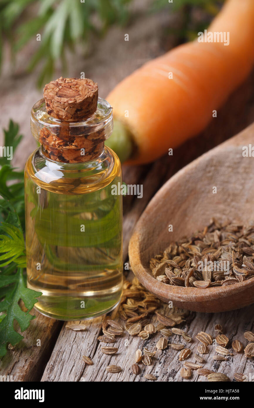 The essential oil of carrot seeds in a glass bottle on a wooden table. vertical macro Stock Photo