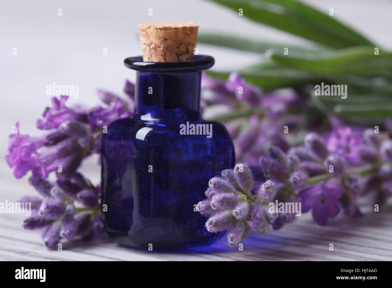 aromatic lavender oil in the blue bottle and flowers on wooden table. Horizontal close-up Stock Photo