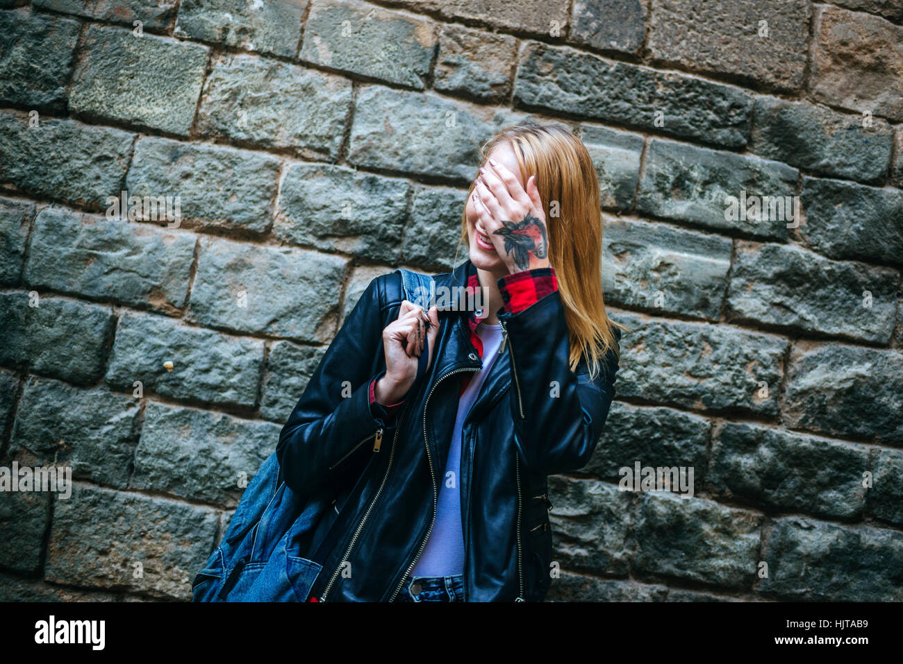 Smiling young woman standing in front of wall covering face with her ...