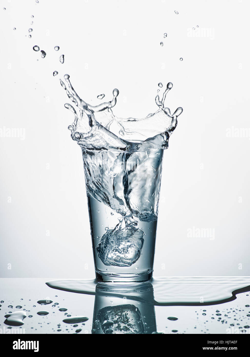 Glass with sinking ice cube and splashing water in front of white