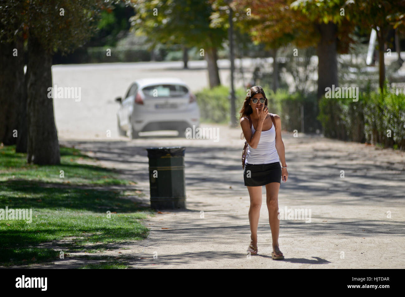 Brunette woman in mini skirt walking down the street, with a car on the background Stock Photo