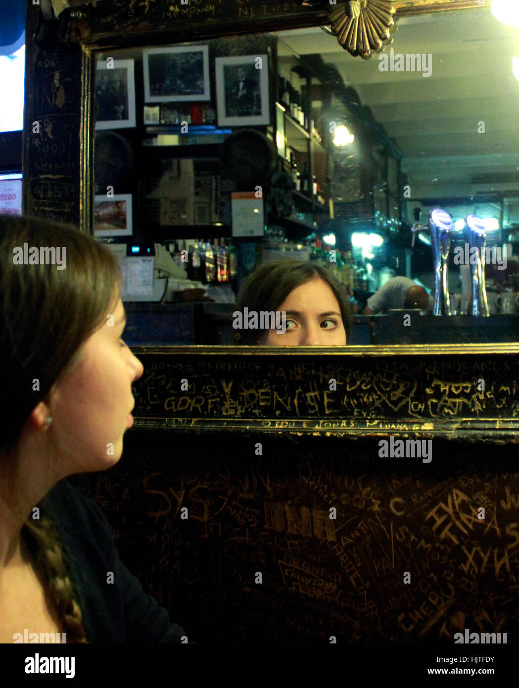 Girl looking her eyes on a mirror sitting in an old cafe in San Telmo, Buenos Aires. Stock Photo