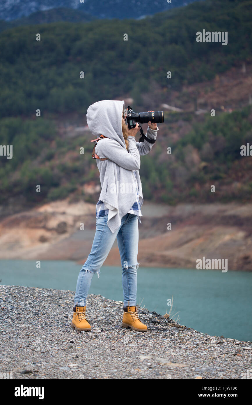 Full length portrait of young woman photographing landscape using long range lens and dressed in grey hoodie Stock Photo