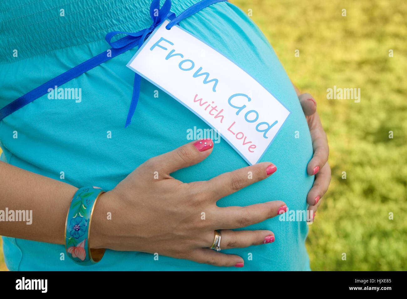 Expecting Mom's hands on tummy with card 'From God with Love' Stock Photo