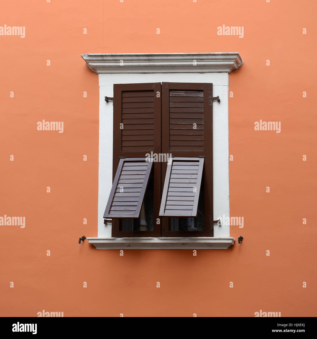 Stone-framed window with closed but partly opened brown shutters. Stock Photo