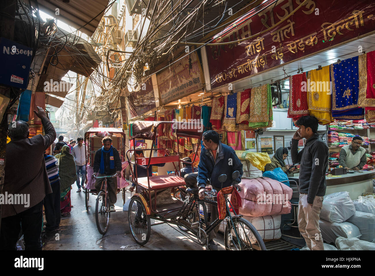 Cycle rickshaw drivers pass a sari shop on a busy and narrow lane in New Delhi's famous Chandni Chowk market, India. Stock Photo