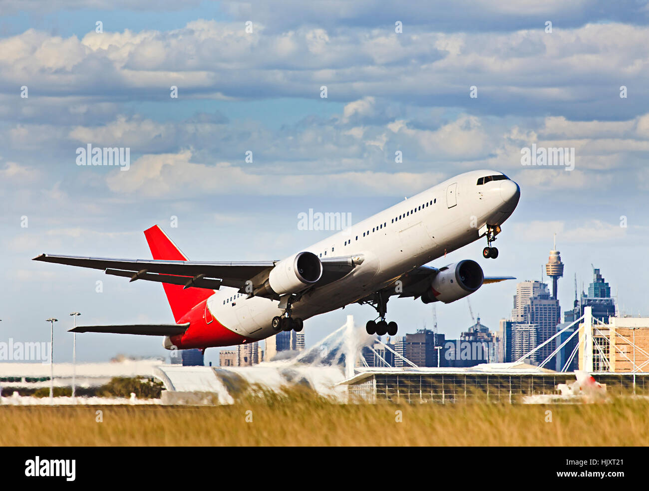 Modern passenger airplaine taking off from airport airfield against Sydney city CBD buildings and towers towards blue sky. Stock Photo