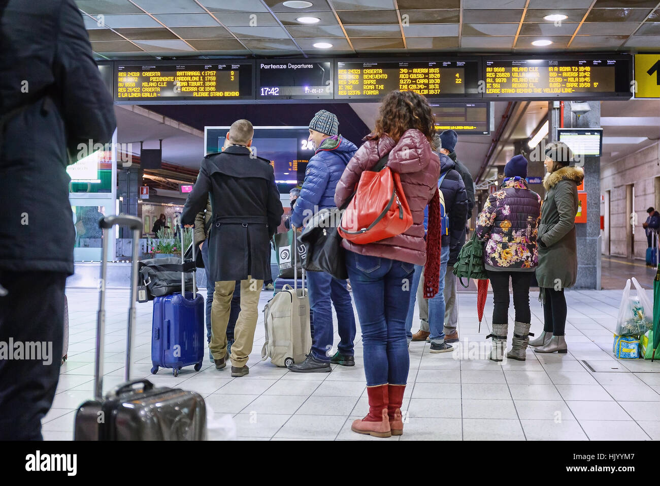 Naples, Italy - January 17, 2017: Some passengers with luggage waiting for the arrival of the train, watching the board of arrivals / departures Stock Photo