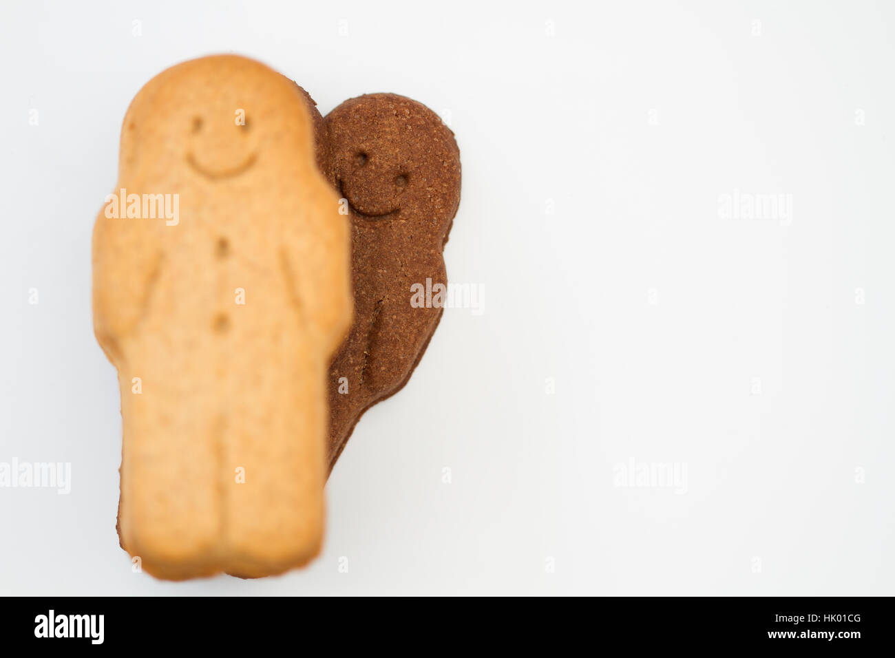 A cheeky black gingerbread man peeking over the shoulder of a white gingerbread man and having fun on a white background. Stock Photo