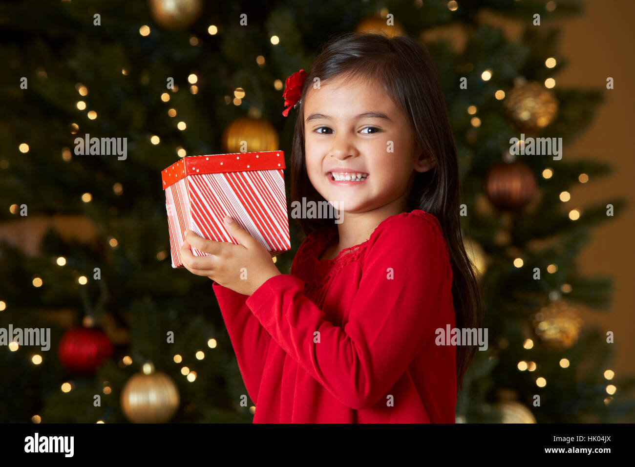 Girl Holding Christmas Present In Front Of Tree Stock Photo - Alamy