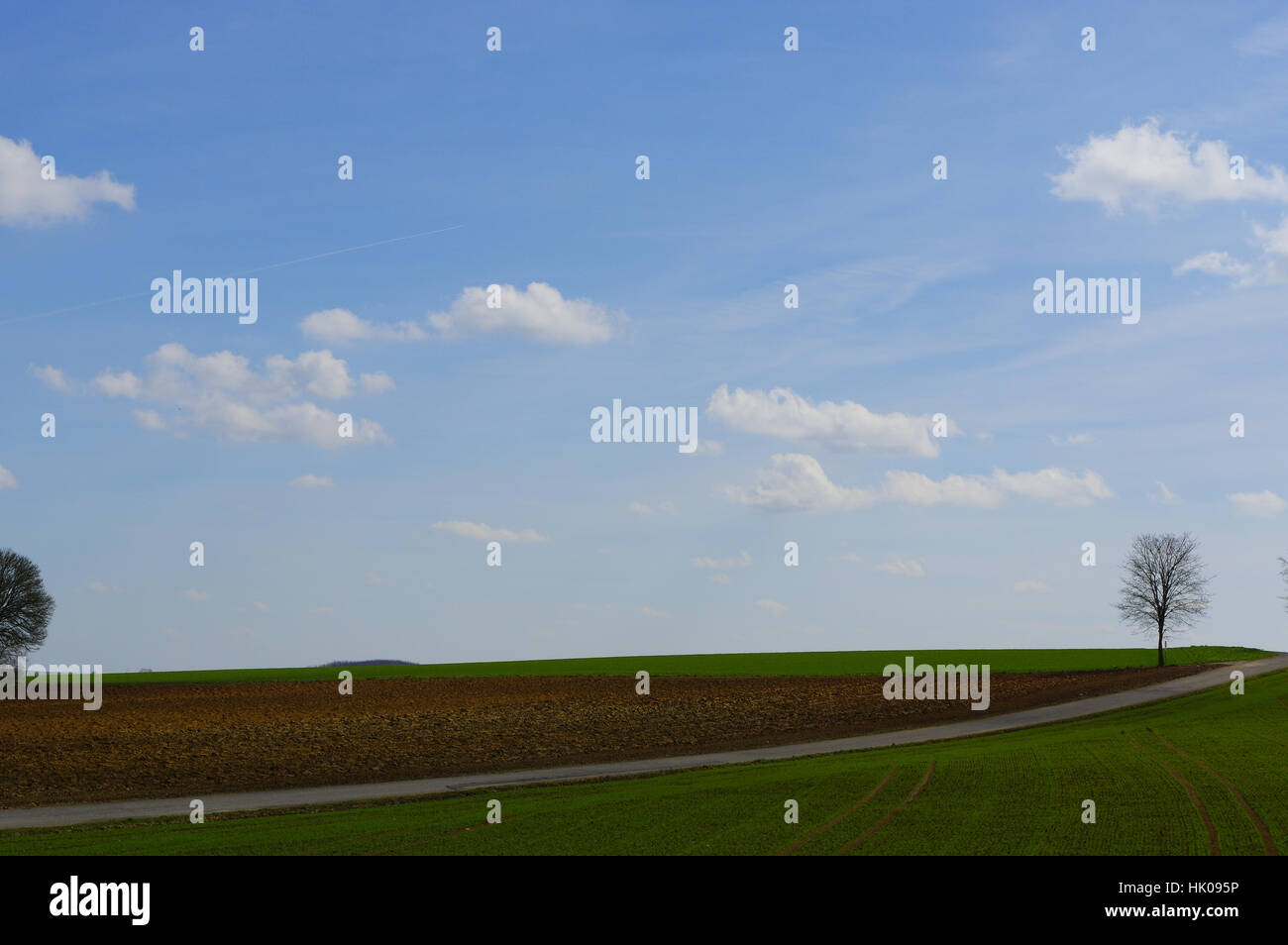 a field under a cloudy sky with a road Stock Photo - Alamy