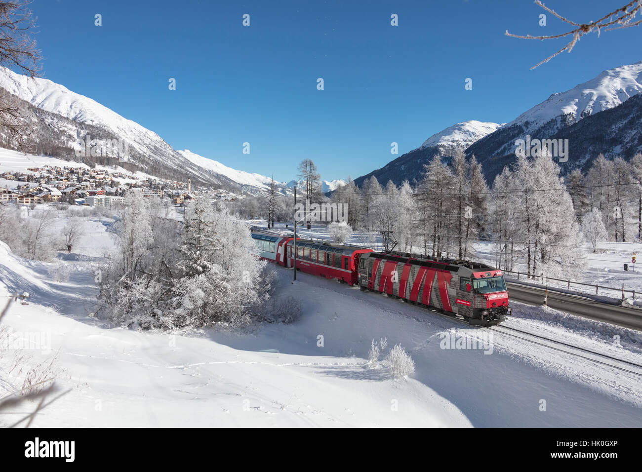 The red train runs across the snowy landscape around Samedan, Maloja, Canton of Graubunden, Engadine, Switzerland Stock Photo